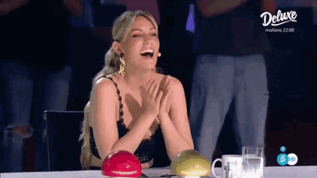 a woman is laughing while sitting at a table in front of a deluxe logo