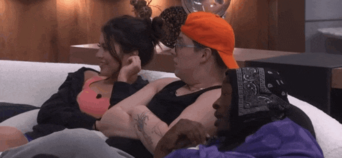 three people sitting on a couch with one wearing a bandana