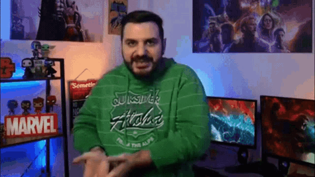 a man wearing a green quiksilver hoodie is standing in a room with a lot of posters on the wall .