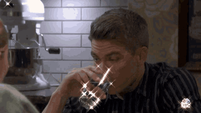 a man drinking from a glass with a nbc logo on the bottom