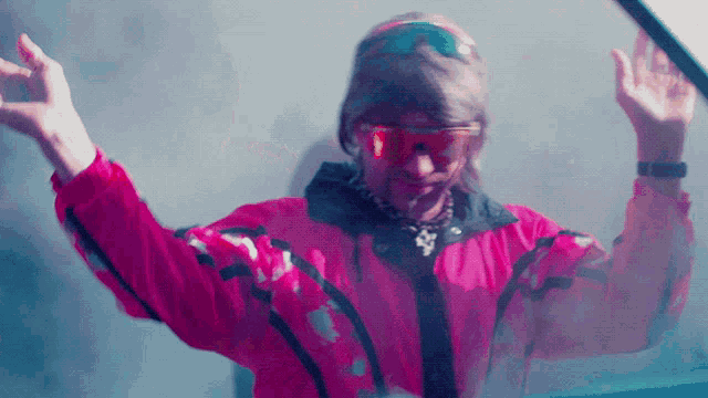 a man wearing a pink jacket and sunglasses holds his arms up