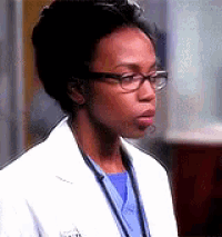 a woman wearing glasses and a white coat is standing in front of a glass of beer .