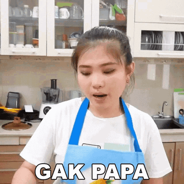 a woman wearing an apron is standing in a kitchen and says " gak papa " on the bottom