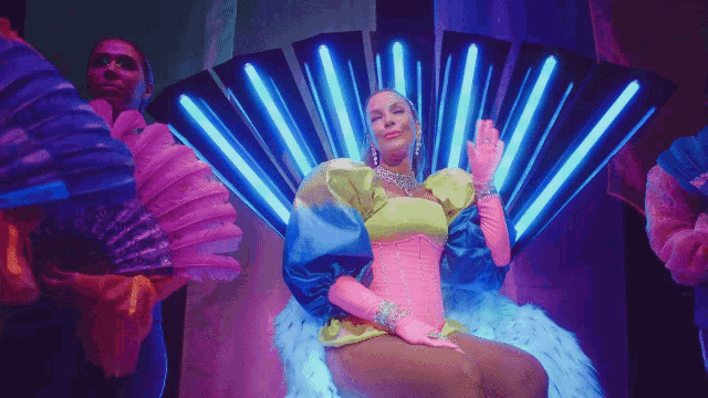a woman in a brightly colored costume is sitting in front of a fan
