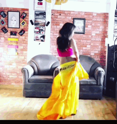 a woman in a yellow skirt is dancing in front of a grey couch