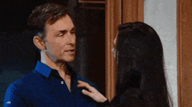 a man in a blue shirt is being kissed by a woman in a black shirt .