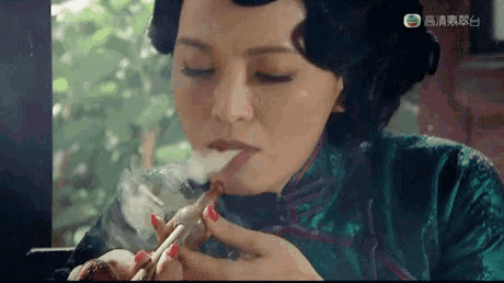 a woman in a green dress is smoking a cigarette with red nails on her nails .
