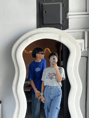 a couple taking a picture in front of a large mirror
