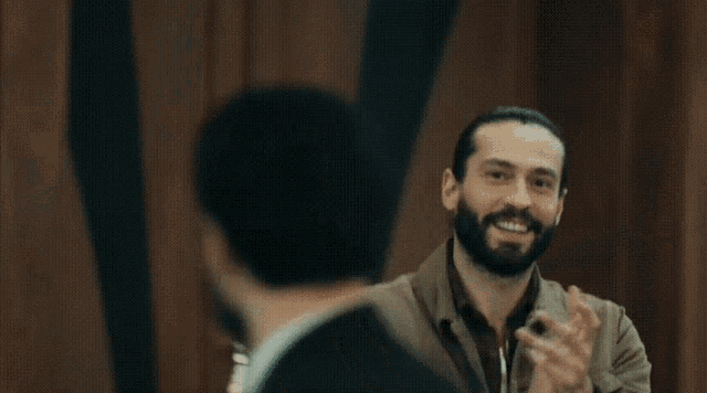 a man with a beard is smiling and clapping his hands in a dark room .