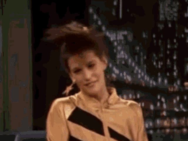 a woman wearing a yellow and black striped shirt is dancing in front of a bridge .