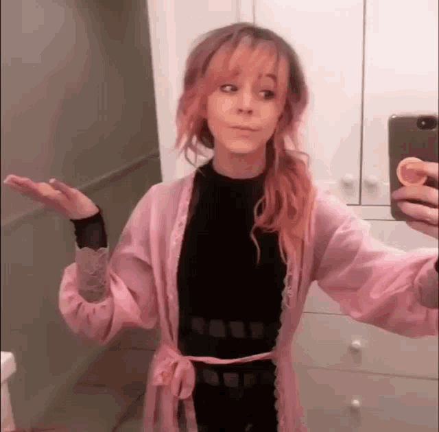 a girl with pink hair is taking a selfie in a bathroom .