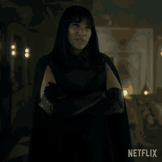 a woman in a black cape and gloves is standing with her arms crossed in front of a sign that says netflix