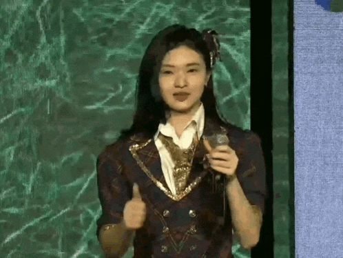 a young woman is holding a microphone and giving a thumbs up .