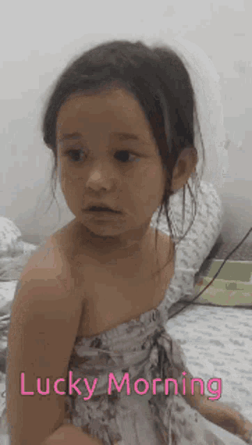 a little girl is sitting on a bed with the words lucky morning written below her