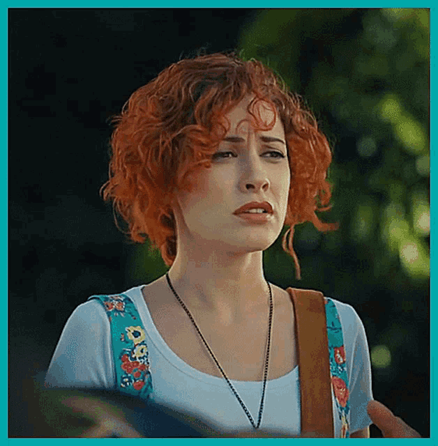 a woman with red curly hair wearing a white shirt and overalls