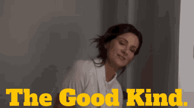 a woman in a white shirt is smiling in front of a sign that says the good kind