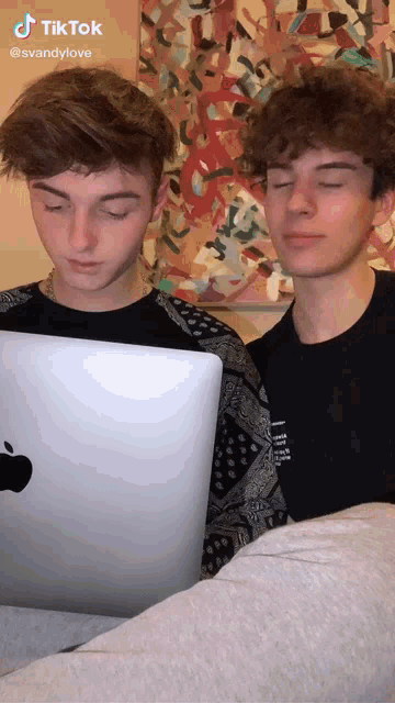 two boys are looking at an apple laptop together
