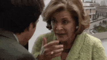 a woman in a green jacket is talking to a man in a suit in a room .