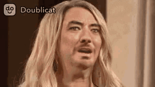 a man with blonde hair and a beard is wearing a wig and making a funny face .