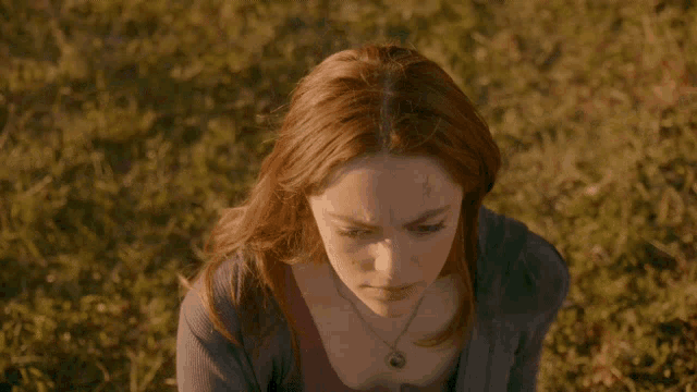 a woman with long red hair is sitting in a grassy field