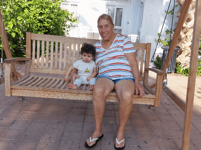 an elderly woman sits on a wooden swing with a baby on her lap