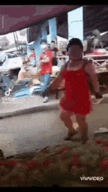 a woman in a red dress is walking down the street in front of a crowd of people .