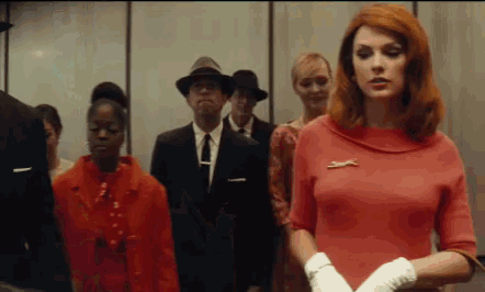 a woman in a red dress stands in front of a group of people in suits