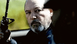 a man with a beard is holding a gun in a car and looking at the camera .