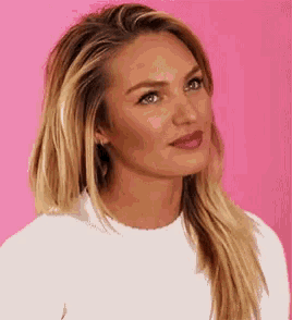 a close up of a woman 's face with long blonde hair and a white shirt on a pink background .