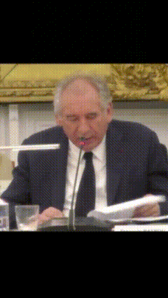 a man in a suit and tie is sitting at a table speaking into a microphone