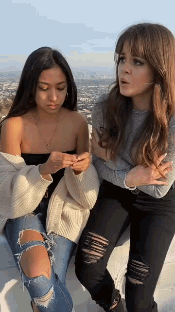 two women are standing next to each other with their arms crossed and one is wearing ripped jeans .
