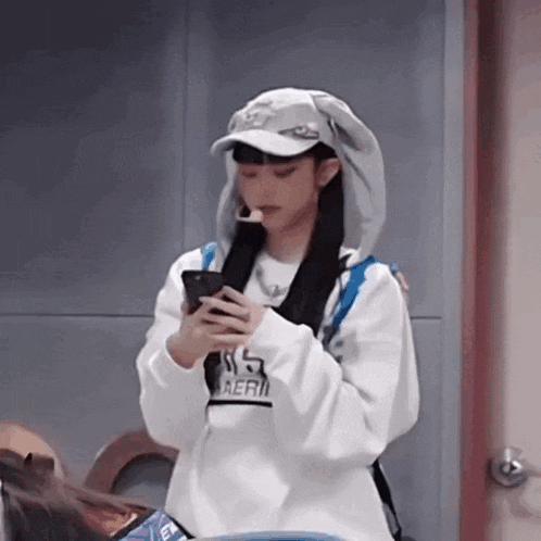 a girl wearing a hoodie and hat is looking at her phone .