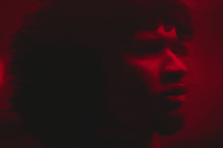 a close up of a man 's face in a dark room with a red light behind him
