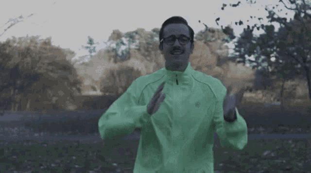 a man wearing a green jacket and glasses is running in a park