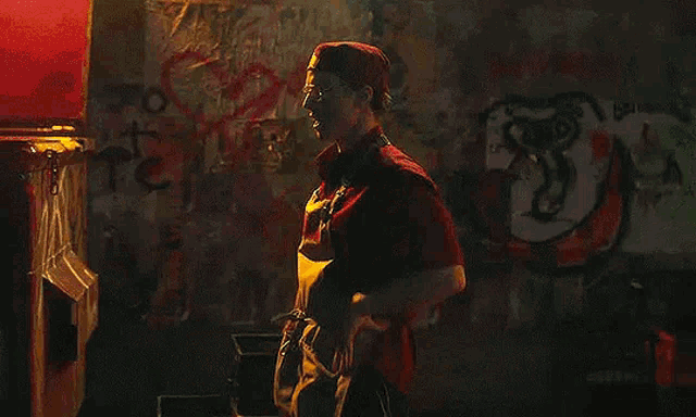 a man in a red hat and apron is standing in a dark alleyway .