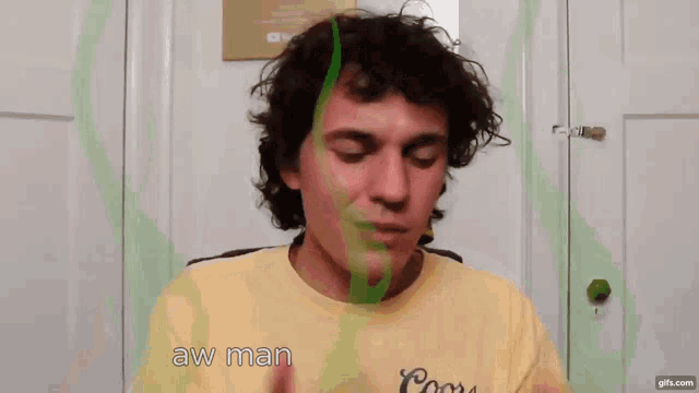 a man wearing a yellow coors shirt is making a face