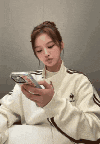 a woman in a white adidas jacket holds a cell phone