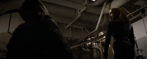 a man in a black suit is standing in a dark room with ropes hanging from the walls .