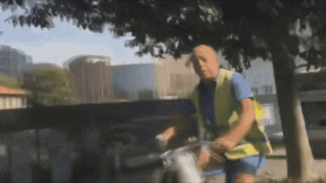 a man wearing a blue shirt and a yellow vest rides a bike