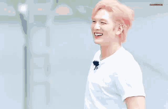 a young man with pink hair is smiling and wearing a white shirt .