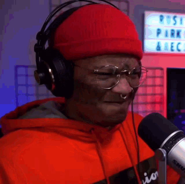 a man wearing headphones , glasses and a red hat is talking into a microphone .