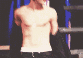 a man without a shirt is standing on a stage with a microphone on his head .
