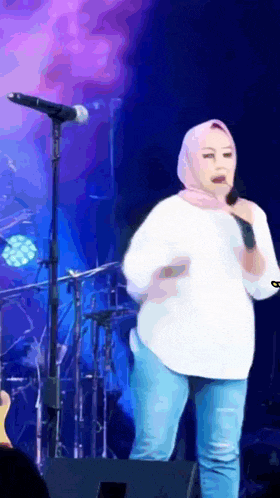 a woman in a hijab is singing into a microphone on a stage