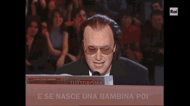 a man wearing sunglasses is sitting at a piano with the words " e se nasce una bambina poi " written on the keyboard