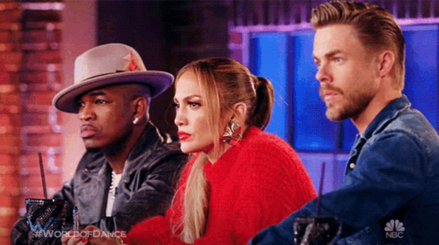 a woman in a red sweater sits between two men in hats on a nbc show called world of dance