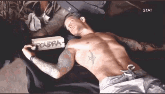 a shirtless man laying on a bed next to a box that says poudra on it