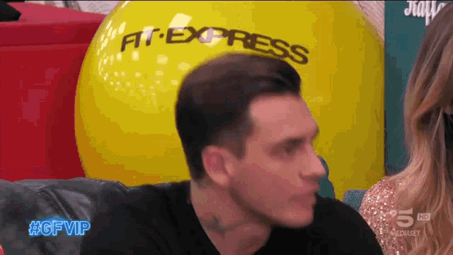a man sits in front of a large yellow ball that says fit express