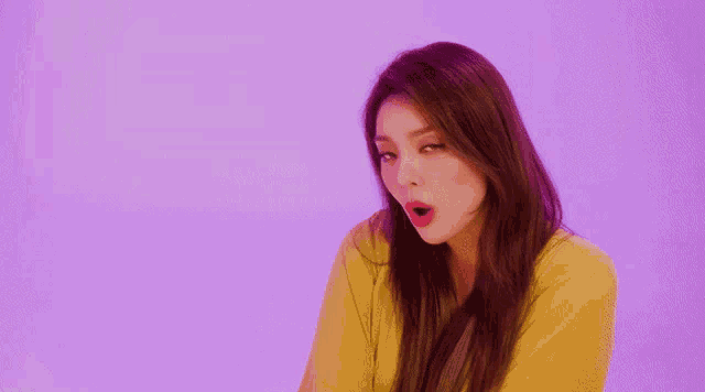a woman in a yellow shirt is standing in front of a purple background .
