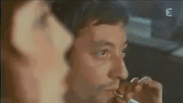 a man is smoking a cigarette while a woman looks on in a blurry photo .