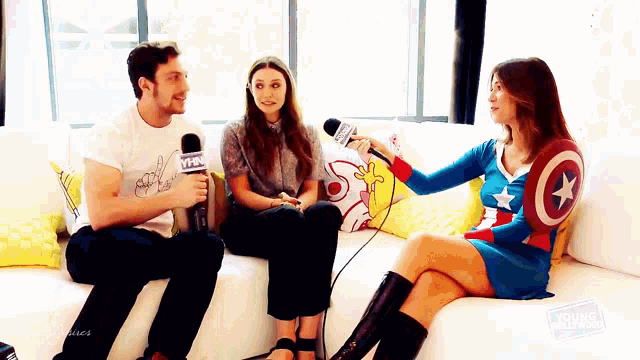 a woman in a captain america costume is sitting on a couch talking to two people .